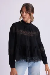Blusa negra con cuello alto y mangas largas, con detalles de encaje en el pecho, mangas y ruedo.