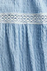 Blusa celeste con textura arrugada, cuello redondo, mangas cortas con volados y detalles de encaje blanco en el canesú y los bordes de las mangas.