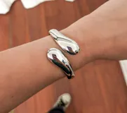 Brazalete rígido plateado con forma de gota en los extremos.