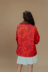 Campera tipo parka reversible con estampado de flores rojas y naranjas sobre fondo rojo, cuello marrón y bolsillos frontales.