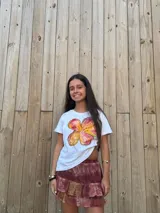 Remera blanca de algodón con mangas cortas y estampado de flor pintada a mano en tonos naranja, amarillo y rosa.