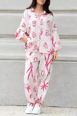 Conjunto de camisa de manga larga y pantalón largo, ambos con estampado abstracto en tonos rosa sobre fondo blanco. Camisa de corte oversized con cuello clásico y cierre frontal con botones. Pantalón con bolsillos laterales.