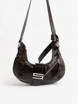Cartera marrón oscuro con forma de medialuna, con correa de hombro ajustable, cierre superior con cremallera y detalle de hebilla metálica en la parte delantera.