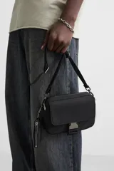 Bandolera negra de tela técnica con correa ajustable y extraíble. Tiene un compartimento principal con cierre de cremallera, un bolsillo interior con cremallera, un bolsillo frontal con solapa y hebilla de liberación rápida, y un monedero removible.