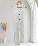 Chaleco largo sin mangas, color blanco, tejido a crochet con patrón geométrico. Presenta cuello en V y cierre frontal con botones marrones.