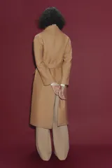 Abrigo largo color camel confeccionado en hilatura con lana. Tiene cuello clásico, cierre frontal con botones ocultos, bolsillos de parche y cinturón del mismo tejido.