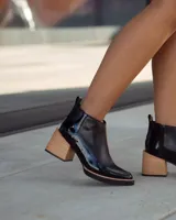 Botín Chelsea de cuero negro charol, con punta cuadrada y taco ancho de madera clara.