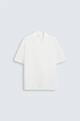 Camisa de calce relajado confeccionada en tejido fluido de mezcla de viscosa, color blanco. Presenta cuello bowling, manga corta, aberturas laterales en el bajo y cierre frontal con botones al tono.