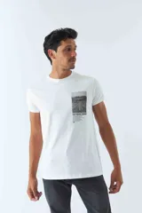 Remera blanca de algodón con cuello redondo y estampado rectangular con imagen de una carretera y texto en el frente.
