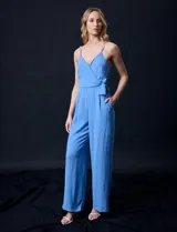 Enterito celeste de crepe marca Luxology, con escote en V cruzado, cintura elastizada, espalda en punto smock y tirantes con detalle de cadenas.