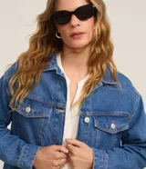 Campera trucker de jeans azul oscuro, corte amplio, con cuello clásico, cierre frontal con botones blancos, mangas largas y bolsillos delanteros con solapa.