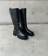 Botas de caña alta color negro, de cuero, con suela track y detalles de correas con hebillas.