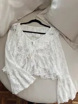 Blusa de encaje blanco con volados en el escote y mangas acampanadas. Se ata en el frente con lazos.