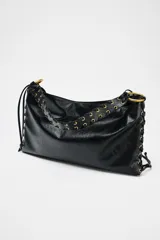 Bolso de hombro alargado color negro, con detalle de pasados metálicos en los laterales y asa trenzada. Tiene doble bolsillo interior con cremallera y cierre mediante botón imantado.