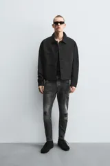 Pantalón de jean negro ajustado al cuerpo desde la cintura hasta el tobillo, de tiro medio y tejido elástico. Diseño de cinco bolsillos con lavado efecto roto y cierre frontal con cremallera y botón.