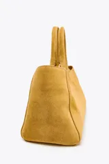 Bolso mini city color mostaza de serraje, con asa de mano y asa bandolera extraíble. Tiene un bolsillo interior con cremallera y cierre mediante botón imantado.