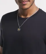 Collar plateado con cadena de eslabones y colgante redondo gris con detalle de carita sonriente dorada.