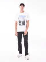 Remera blanca de corte recto con estampa fotográfica de edificios en la parte frontal.