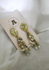 Aros colgantes con base dorada y apliques de piedras irregulares en tonos verde claro y blanco.