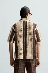 Camisa de hombre de corte relajado, confeccionada en tejido de crochet con estructura abierta. Presenta cuello bowling, manga corta y cierre frontal con botones.