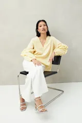 Blusa color amarillo pálido de manga larga con escote en V, mangas abullonadas con volados y botones forrados.