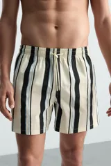 Bañador de hombre confeccionado en tejido técnico, color blanco con rayas verticales negras y celestes. Cuenta con cintura elástica ajustable con cordón, bolsillos laterales, bolsillo trasero y forro interior.