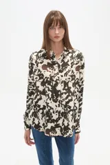 Camisa holgada de manga larga, color negro, con cuello camisa y botones frontales. Presenta apliques de tachas plateadas en los hombros y a lo largo de la tapeta frontal.