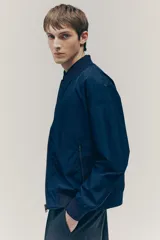 Campera bomber azul marino con cuello elevado acanalado y cierre frontal. Tiene bolsillos laterales y un bolsillo interior, todos con cierre. Los puños y el bajo son acanalados. Está forrada.