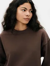 Buzo de tejido de punto color gris melange, con cuello redondo y corte holgado. Presenta costuras visibles en los hombros y puños y cintura acanalados.