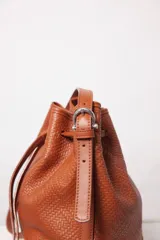 Cartera tipo botellero de cuero negro con efecto trenzado, tamaño mediano, cierre con frunce, correa ajustable con hebillas para usar al hombro o cruzada, doble bolsillo interior (uno con cierre) y forro de algodón.