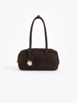 Cartera tipo baguette color marrón oscuro, confeccionada en cuero descarne vacuno. Presenta un gofrado con las iniciales "JCH" en la parte delantera y un charm colgante de mariquita dorada en un tag de cuero. Tiene una manija del mismo material y una estructura firme.