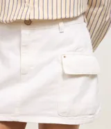 Minifalda cargo color blanco, confeccionada en sarga de algodón, con trabillas, bolsillos laterales y cierre frontal con botón.