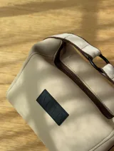 Neceser color beige de forma rectangular, con cierre superior y asa de mano.