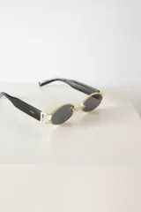 Lentes de sol ovalados con marco dorado y patillas negras.