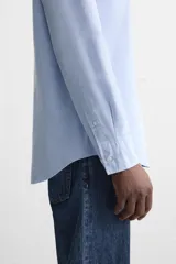 Camisa celeste de algodón, corte relaxed fit, cuello abotonado, manga larga con puños abotonados y cierre frontal con botones.