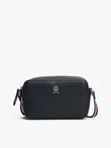 Cartera cruzada tipo cámara de poliuretano color azul marino, con cierre principal de cremallera y monograma TH metálico dorado al frente. La correa larga es ajustable y presenta la cinta distintiva de la marca en rojo, blanco y azul.