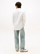 Camisa blanca de manga larga, confeccionada en mezcla de algodón y lino. Tiene corte regular, cuello abotonado, cierre con botones y logo de Tommy Jeans bordado en el pecho.