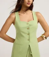 Chaleco sastrero color verde lima, con escote cuadrado y detalle de corazón en el busto, abotonado al frente con botones dorados. Presenta pinzas delanteras y bolsillos falsos.