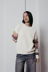 Sweater de punto color crema con cuello redondo y mangas largas con diseño geométrico en tonos beige, rojo, azul y blanco.