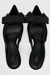 Zapato destalonado de terciopelo negro con tacón fino y adorno de lazo en la parte delantera.