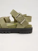 Sandalias romanas color verde oliva, con tiras entrecruzadas y hebilla lateral. Suela de goma negra con plataforma de 3cm. Fabricadas en cuero vacuno.