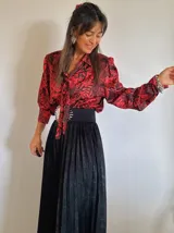 Blusa de manga larga con estampado de flores rojas y negras, cuello con lazo y corte holgado.