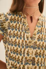 Vestido corto color crema con estampado floral en tonos azul y ocre. Tiene escote en V, mangas cortas con volados y falda con volados y terminación con guarda azul.