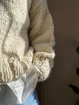 Sweater tejido de lana merino color crudo, con cuello alto y mangas largas abullonadas. Tejido artesanal con punto grueso.