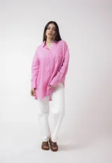 Camisa blanca de lino, de corte holgado, con cuello clásico, cierre frontal con botones, bolsillo en el pecho y mangas largas con puños abotonados.