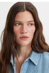 Camisa de denim celeste de manga larga con cuello clásico, cierre frontal con botones a presión, dos bolsillos en el pecho con solapa abotonada y corte recto.