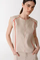 Blusa color beige de lino con cuello redondo y mangas cortas. Presenta vivos y pespuntes a contratono en color rojo.