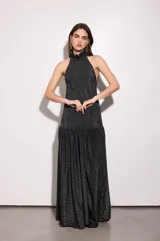 Vestido largo negro con finas líneas plateadas, de corte holgado, escote halter y espalda baja. Presenta volados en el cuello y en la cadera.