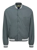 Campera bomber casual color gris verdoso, con cuello tipo baseball y puños de canalé a rayas blancas. Cierre con botones a presión y bolsillos frontales. Confeccionada en tejido liviano y transpirable con hombros caídos.
