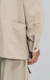 Camisa beige de manga larga, estilo técnico con múltiples bolsillos delanteros y un bolsillo en la parte inferior de la espalda, botones en la cartera y mangas, calce oversize, confeccionada en textil ligero suave al tacto.